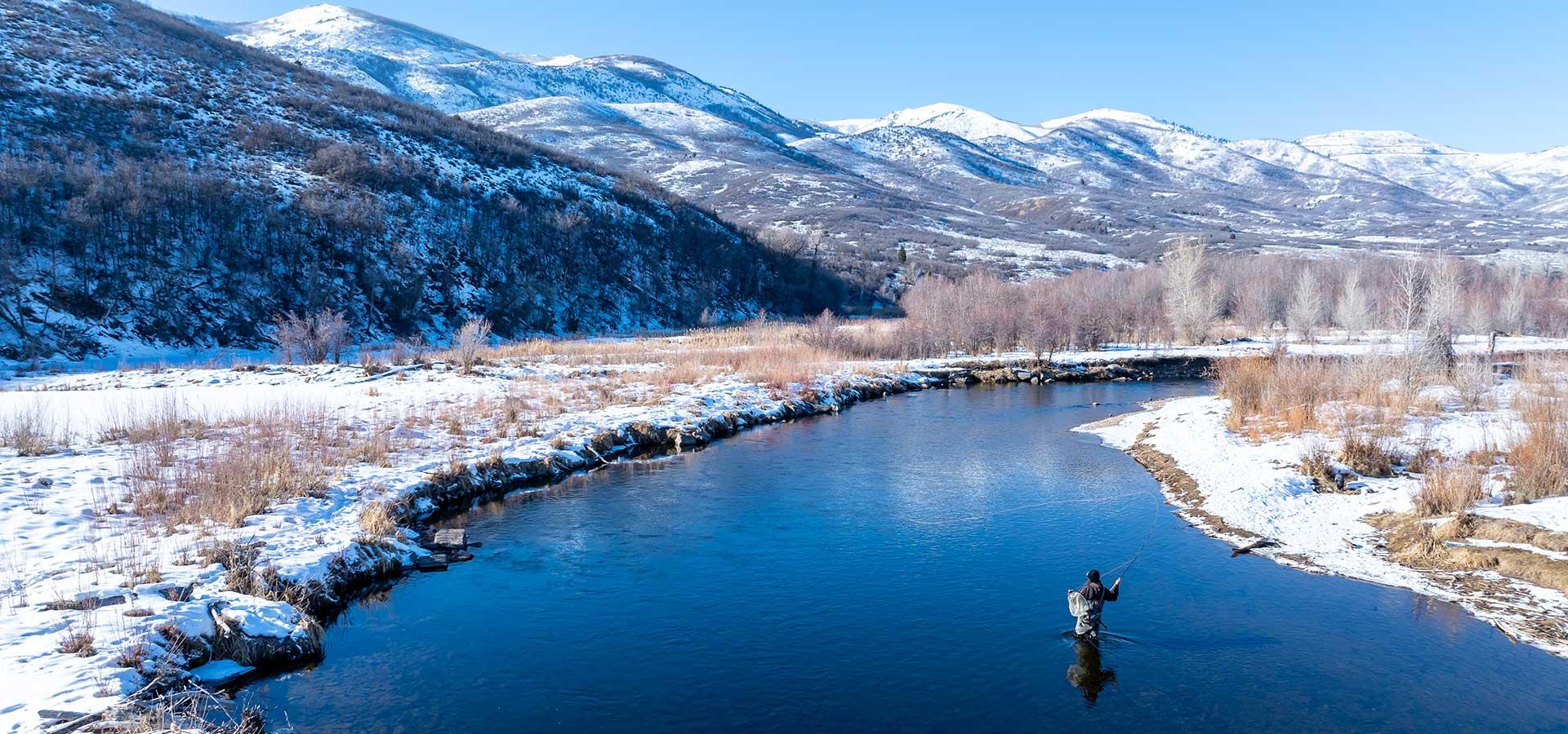 Jans Expert fishing on a river during winter with snow on the banks and mountains in the background in northern Utah.