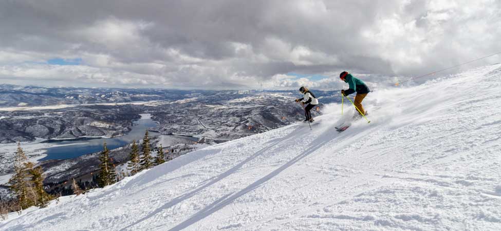 A male and female skier make their way down Stein’s Way overlooking Jordanelle Reservoir at Deer Valley Resort.