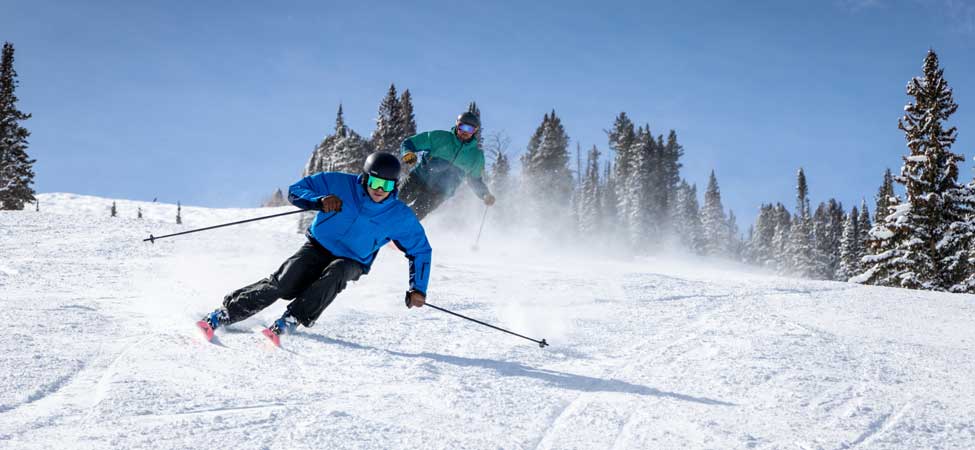 Two male skiers carve a turn on a groomer at Solitude Mountain Resort.