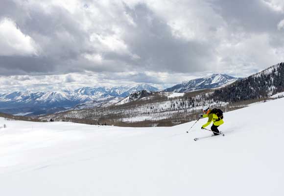 Mark Fischer skis down Empire pass with a view of Heber Valley.