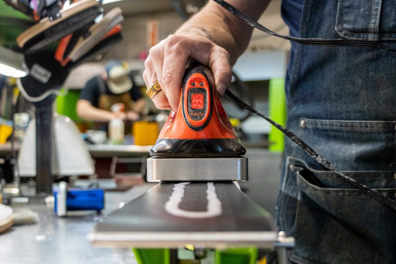 Ski technician waxes a pair of skis.