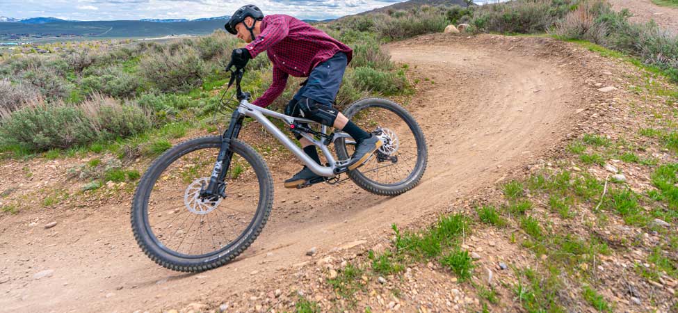 dappled sunlight falls on a mountain biker who leans into a corner