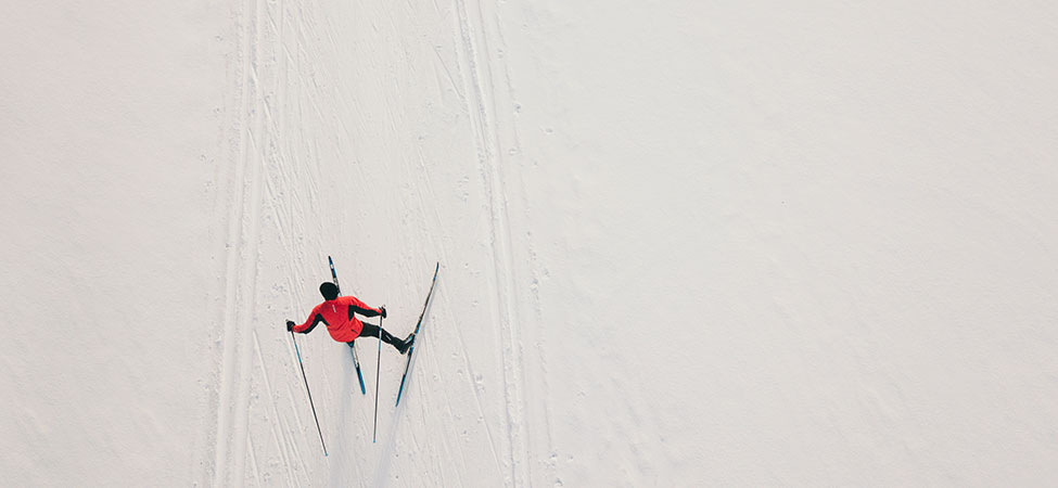 overhead view of a skate skier in action, wearing a red jacket, surrounded by snow