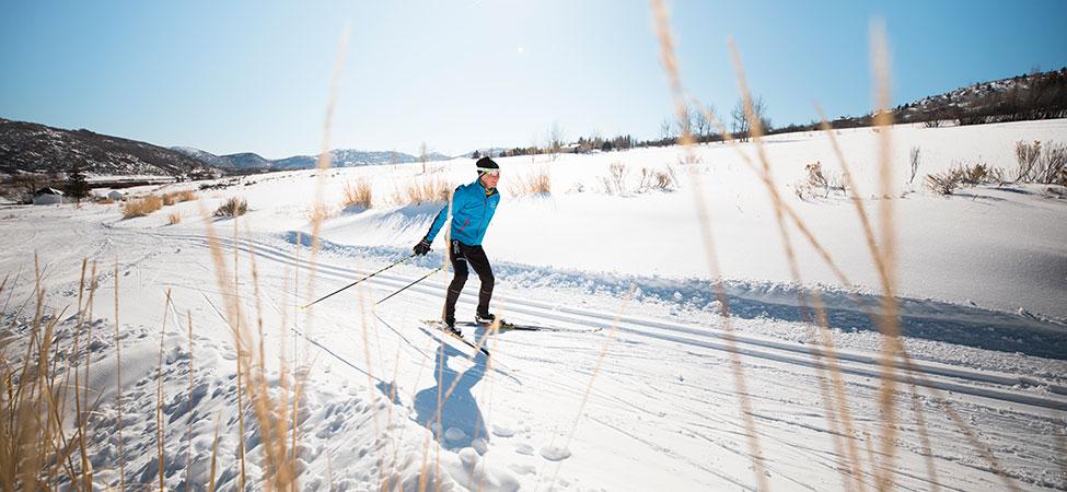 Nordic skier in a blue jacket skates along a groomed trail on a sunny day