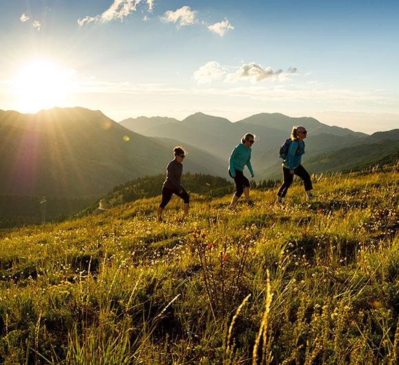 three hikers walk up a grassy hill