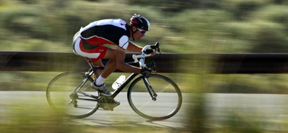 road biker leaned forward as he speeds downhill, with a blurred background