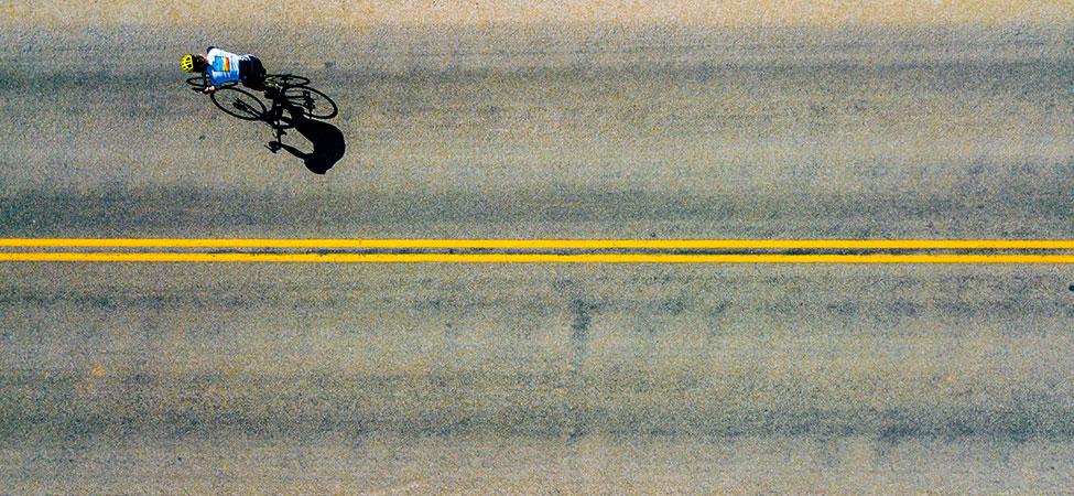 overhead view of a cyclist in a yellow helmet, surrounded by smooth pavement