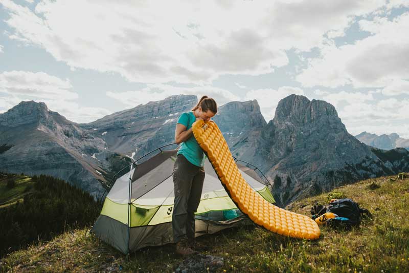 A woman inflates her sleeping pad on a hillside in the backcountry. Image courtesy of Nemo.