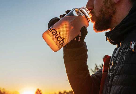 An athlete drinks water mixed with electrolytes in front of a sunset. Image courtesy of Skratch.