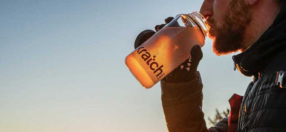 An athlete drinks water mixed with electrolytes in front of a sunset. Image courtesy of Skratch. 