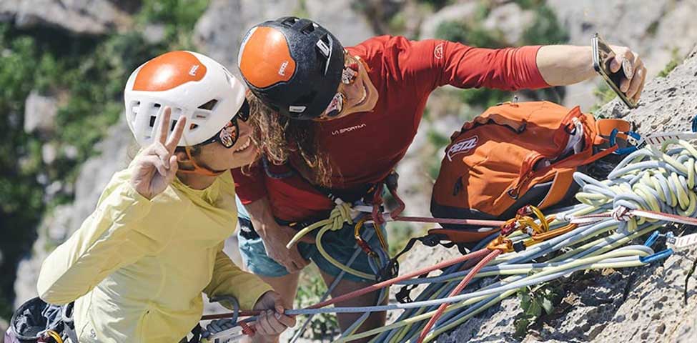 Two climbers wearing plastic shell style helmets take pictures at the anchor. Image courtesy of Petzl.