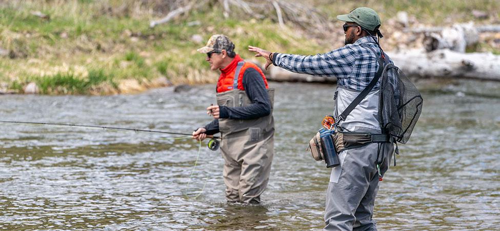fly fishing instructor gives advice to angler student as they wade in a river