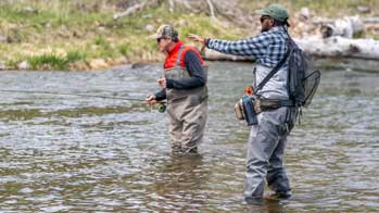 fly fishing instructor gives advice to angler student as they wade in a river