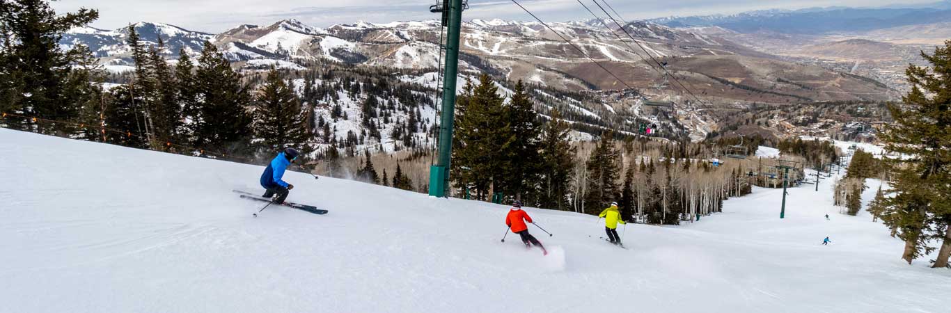 Three skiers on a groomer overlooking Park City, UT.