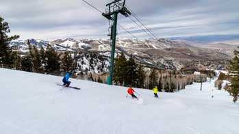 Three skiers on a groomer overlooking Park City, UT.