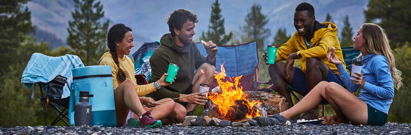 A group of four laugh around a campfire while roasting marshmellows