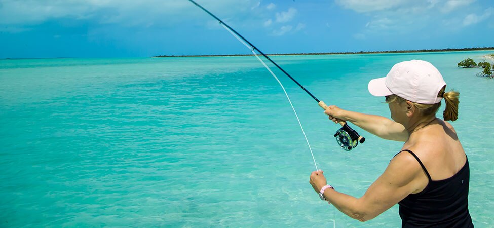 Woman casts a fly rod into clear blue waters.